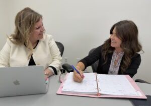 Two women seated at a table, collaborating on work together on a paper and on a laptop